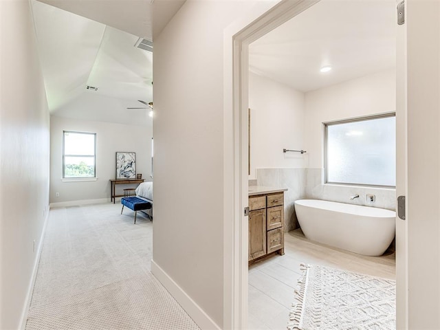 bathroom featuring ceiling fan, vaulted ceiling, a bath, and vanity