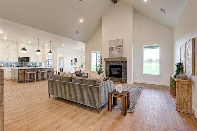 living room featuring light wood-type flooring, a tile fireplace, and high vaulted ceiling