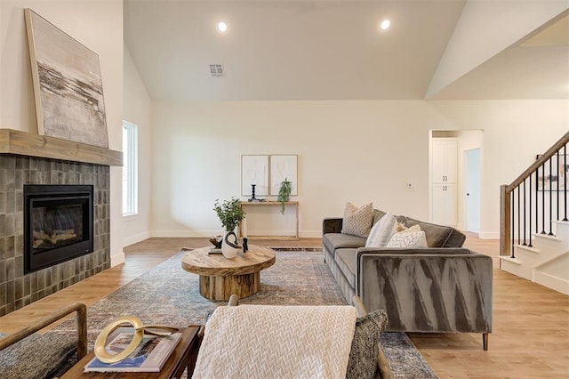 living room with high vaulted ceiling, light hardwood / wood-style flooring, and a tiled fireplace