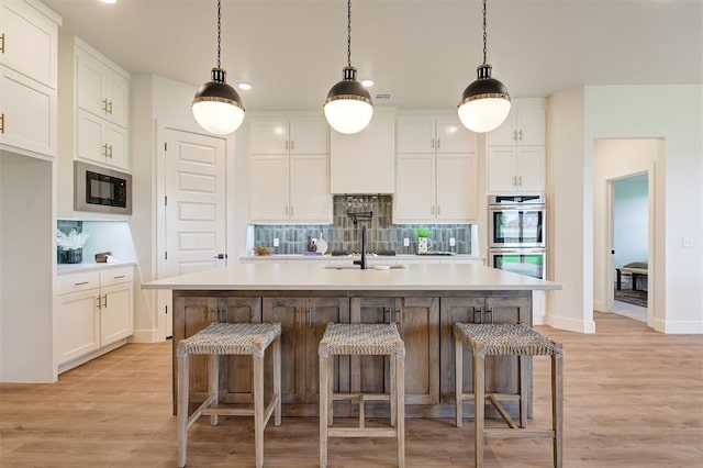 kitchen featuring black appliances, decorative light fixtures, white cabinetry, light hardwood / wood-style floors, and a kitchen island with sink