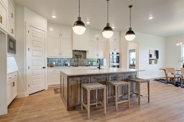 kitchen with light wood-type flooring, white cabinetry, and a center island with sink