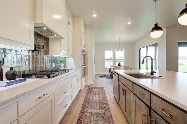 kitchen featuring white cabinetry, stainless steel appliances, sink, premium range hood, and hanging light fixtures