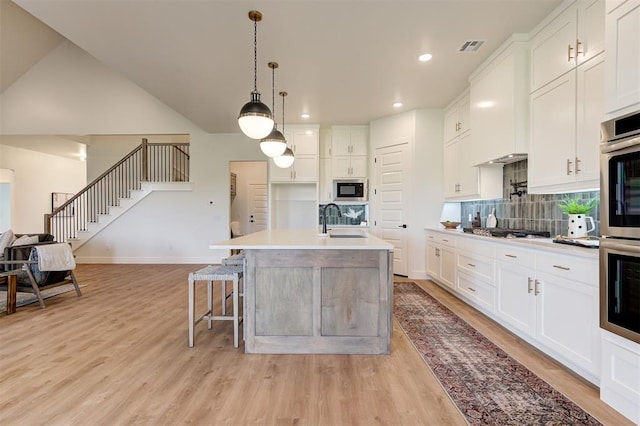 kitchen featuring a center island with sink, sink, hanging light fixtures, stainless steel appliances, and white cabinets