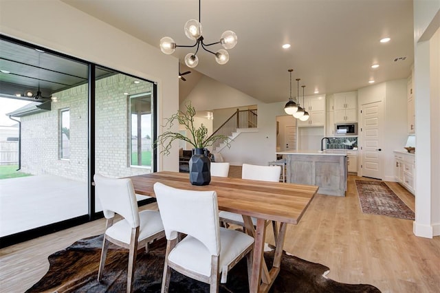 dining area featuring light wood-type flooring, vaulted ceiling, sink, and an inviting chandelier