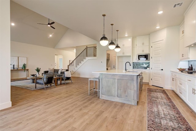 kitchen featuring white cabinetry, sink, hanging light fixtures, a kitchen island with sink, and built in microwave