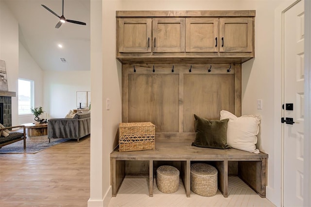 mudroom featuring lofted ceiling, a tiled fireplace, ceiling fan, and light hardwood / wood-style flooring