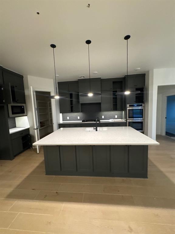 kitchen featuring a large island, hanging light fixtures, backsplash, stainless steel appliances, and light stone counters