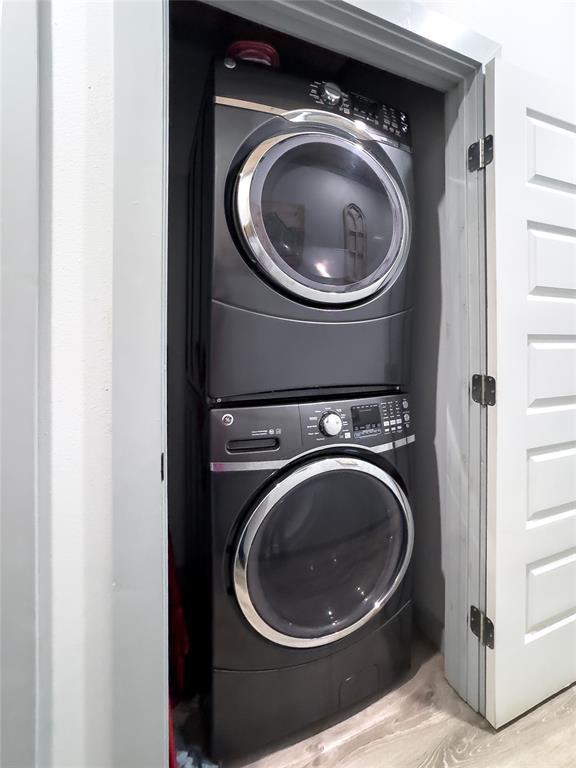 laundry room with light hardwood / wood-style floors and stacked washer / dryer