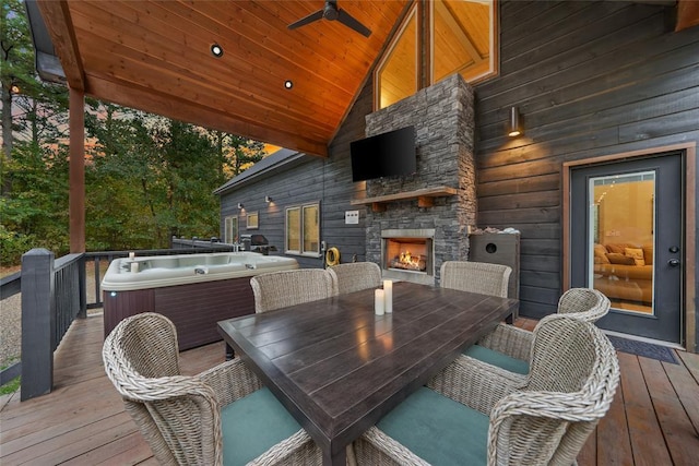 deck with ceiling fan, a hot tub, and an outdoor stone fireplace