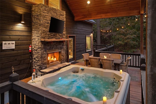 wooden terrace featuring an outdoor stone fireplace and an outdoor hot tub