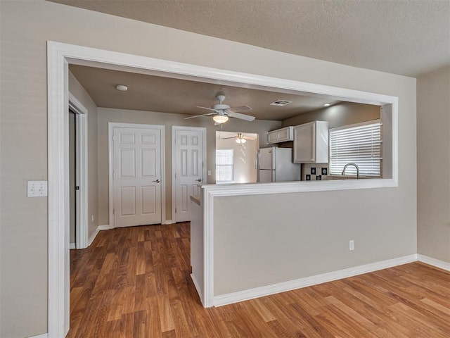 kitchen featuring a textured ceiling, white refrigerator, kitchen peninsula, hardwood / wood-style flooring, and white cabinets