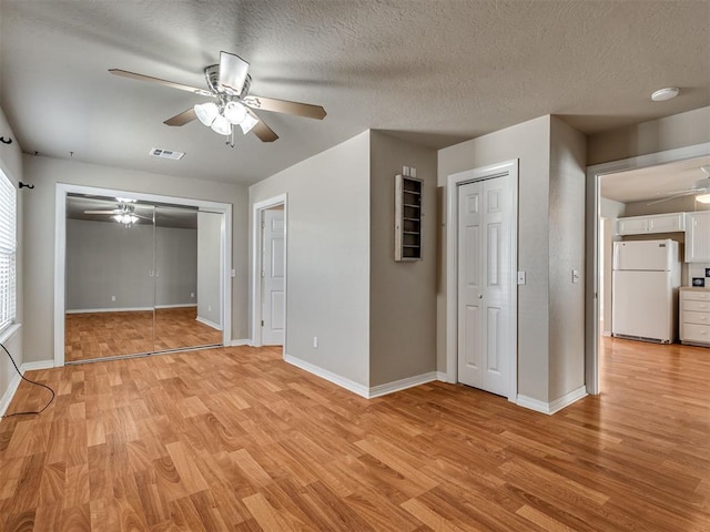 unfurnished bedroom with white refrigerator, light wood-type flooring, a textured ceiling, and ceiling fan