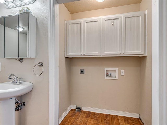 washroom featuring electric dryer hookup, hookup for a washing machine, light hardwood / wood-style floors, and cabinets