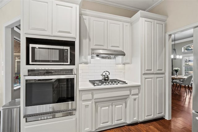 kitchen featuring white cabinetry, crown molding, dark hardwood / wood-style floors, stainless steel appliances, and decorative backsplash