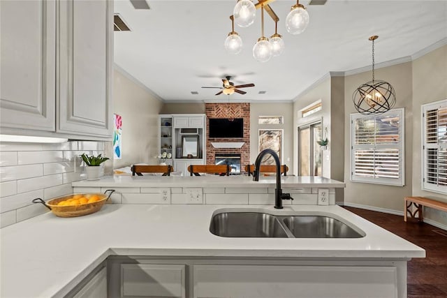 kitchen featuring sink, crown molding, dark wood-type flooring, hanging light fixtures, and a fireplace