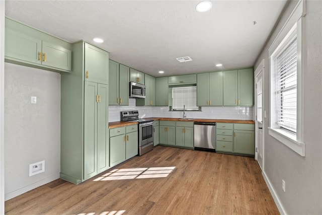 kitchen with appliances with stainless steel finishes, butcher block counters, sink, green cabinets, and light hardwood / wood-style flooring