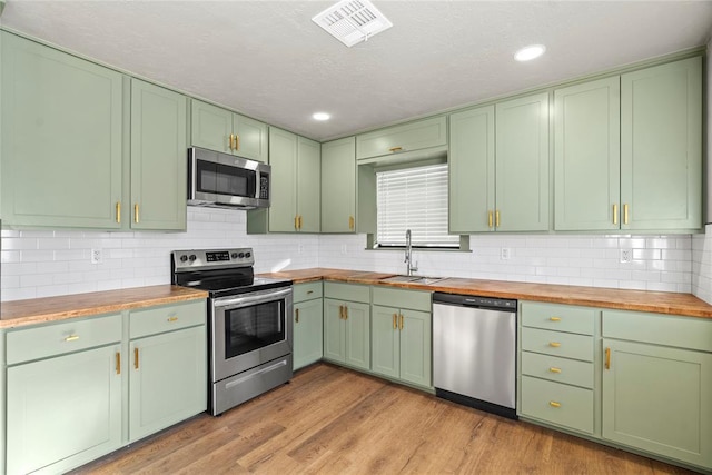 kitchen with butcher block counters, sink, light wood-type flooring, appliances with stainless steel finishes, and green cabinets