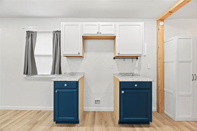 kitchen with white cabinetry, light hardwood / wood-style flooring, light stone counters, and blue cabinetry