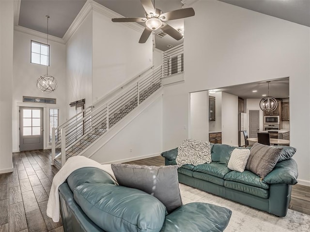 living room with ceiling fan with notable chandelier, a high ceiling, hardwood / wood-style floors, and crown molding