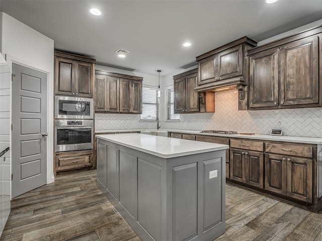 kitchen with decorative light fixtures, dark hardwood / wood-style floors, appliances with stainless steel finishes, and a center island