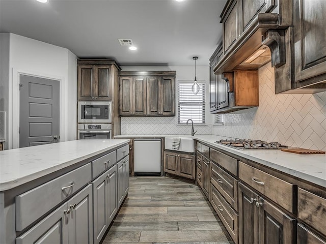 kitchen with dark brown cabinetry, appliances with stainless steel finishes, sink, hanging light fixtures, and light wood-type flooring