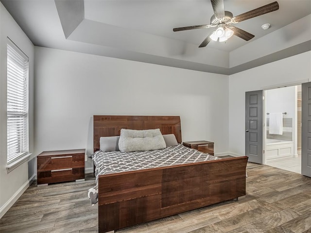 bedroom with ceiling fan, hardwood / wood-style floors, a tray ceiling, and ensuite bath