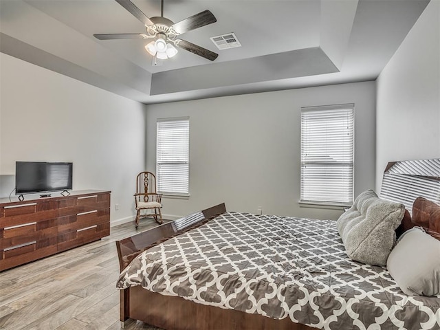 bedroom with ceiling fan, a tray ceiling, and light wood-type flooring