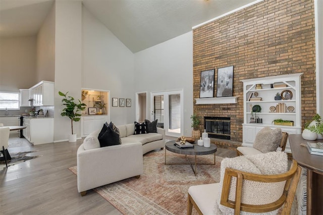 living room with a brick fireplace, sink, light hardwood / wood-style flooring, and high vaulted ceiling