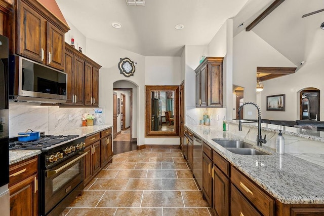 kitchen featuring a sink, backsplash, arched walkways, appliances with stainless steel finishes, and light stone countertops