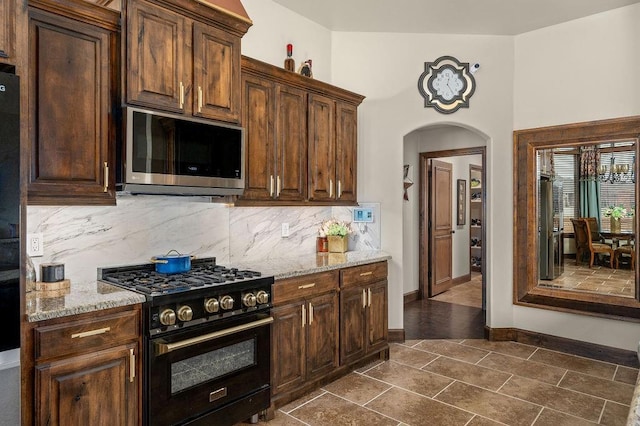 kitchen featuring arched walkways, stainless steel microwave, high end black range, and light stone countertops