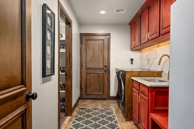 washroom featuring visible vents, stone finish floor, washer and dryer, a sink, and cabinet space