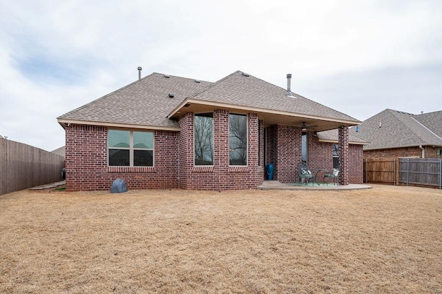 rear view of property featuring brick siding, roof with shingles, a lawn, a fenced backyard, and a patio area