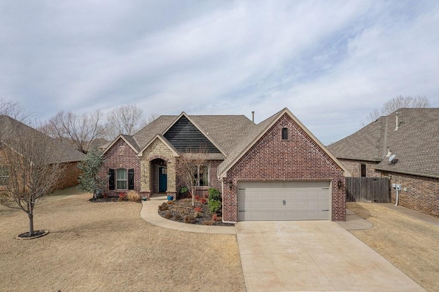 view of front facade featuring driveway, fence, roof with shingles, an attached garage, and brick siding