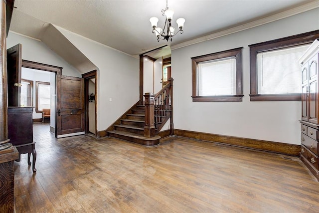 foyer entrance with hardwood / wood-style floors, crown molding, and an inviting chandelier