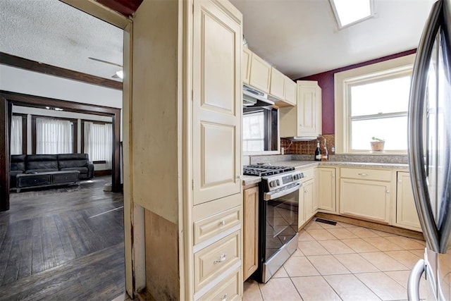 kitchen featuring light tile patterned floors, stainless steel appliances, a textured ceiling, crown molding, and cream cabinets