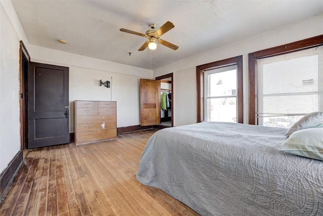 bedroom featuring ceiling fan, wood-type flooring, a textured ceiling, a walk in closet, and a closet