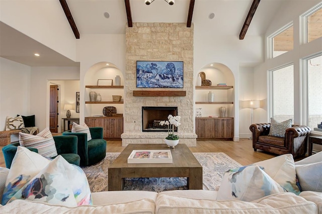 living room featuring light hardwood / wood-style floors, a stone fireplace, built in features, high vaulted ceiling, and beamed ceiling