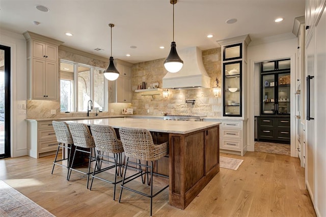 kitchen with premium range hood, light hardwood / wood-style floors, a kitchen bar, and a center island