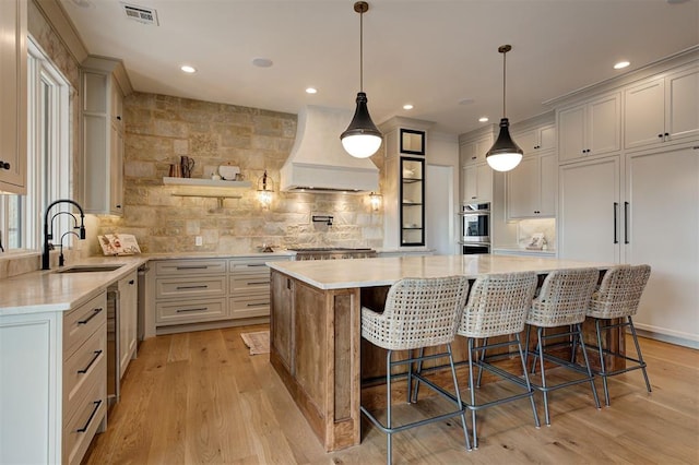 kitchen with decorative light fixtures, premium range hood, sink, light wood-type flooring, and a large island