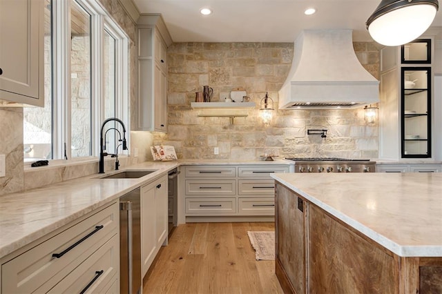 kitchen featuring backsplash, light hardwood / wood-style floors, sink, custom range hood, and light stone counters