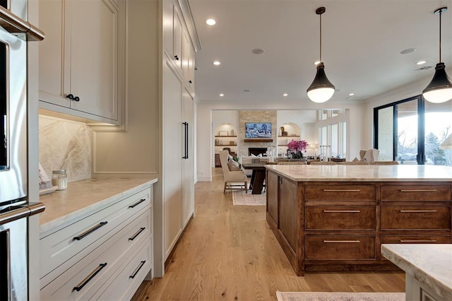 kitchen featuring pendant lighting, white cabinets, a fireplace, decorative backsplash, and light hardwood / wood-style flooring