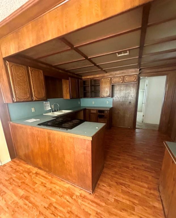 kitchen with sink, kitchen peninsula, black gas stovetop, and light wood-type flooring