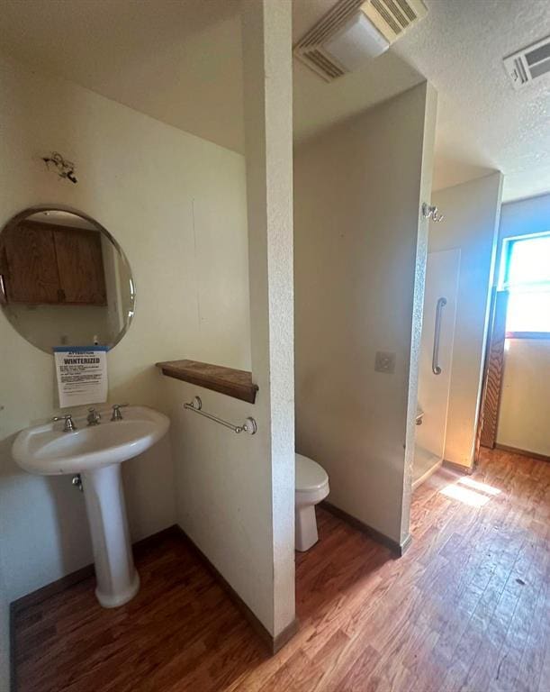 bathroom with hardwood / wood-style flooring, a textured ceiling, toilet, and walk in shower