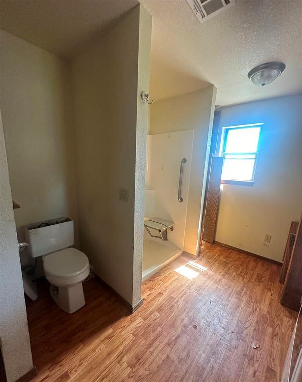 bathroom featuring wood-type flooring, toilet, a textured ceiling, and walk in shower