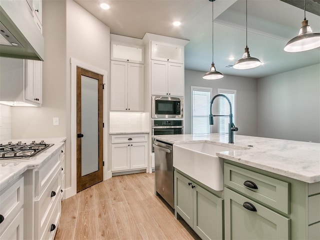 kitchen with under cabinet range hood, stainless steel appliances, a sink, green cabinets, and light wood-type flooring