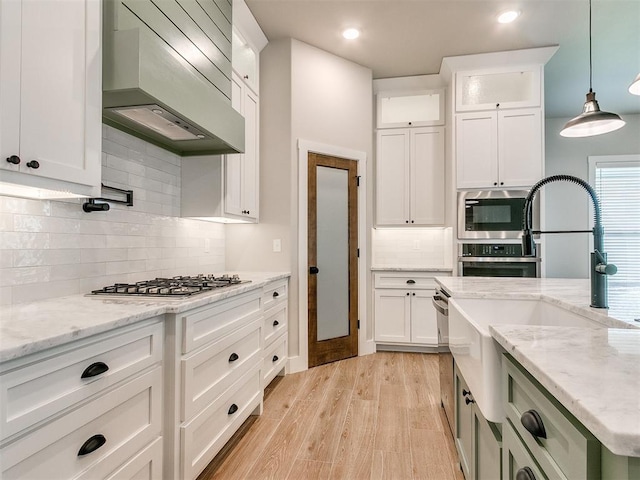 kitchen featuring stainless steel appliances, premium range hood, white cabinets, hanging light fixtures, and light wood-type flooring