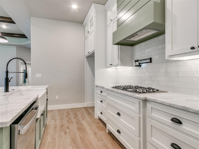 kitchen featuring white cabinetry, light wood-style floors, appliances with stainless steel finishes, decorative backsplash, and wall chimney exhaust hood