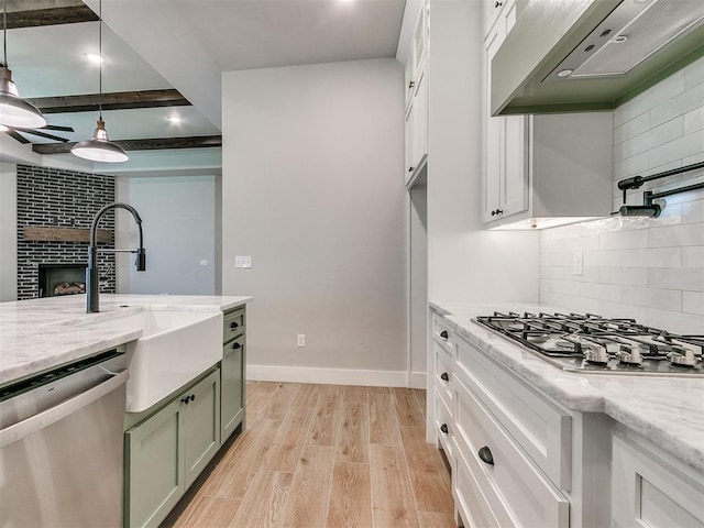 kitchen featuring light wood-style flooring, stainless steel appliances, ventilation hood, a brick fireplace, and decorative backsplash