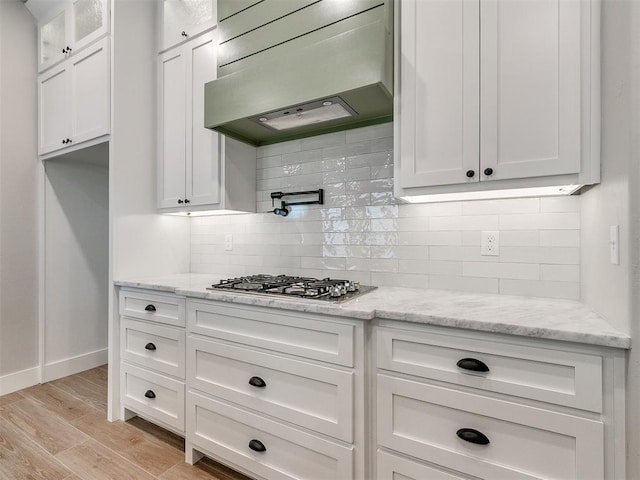 kitchen featuring light stone counters, light wood-style flooring, stainless steel gas cooktop, white cabinets, and custom exhaust hood