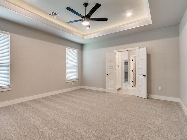 unfurnished bedroom with a tray ceiling, light carpet, visible vents, and baseboards